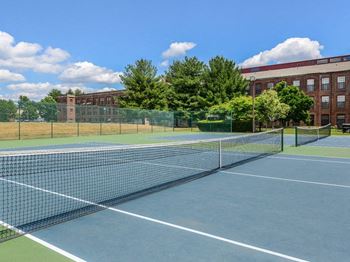 a tennis court with trees and a building in the background at Bigelow Commons, Enfield, Connecticut